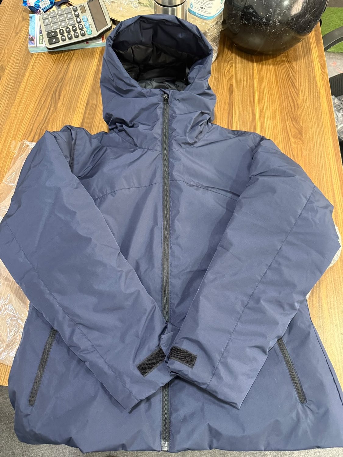 A blue grey down hooded jacket laid on a wooden table