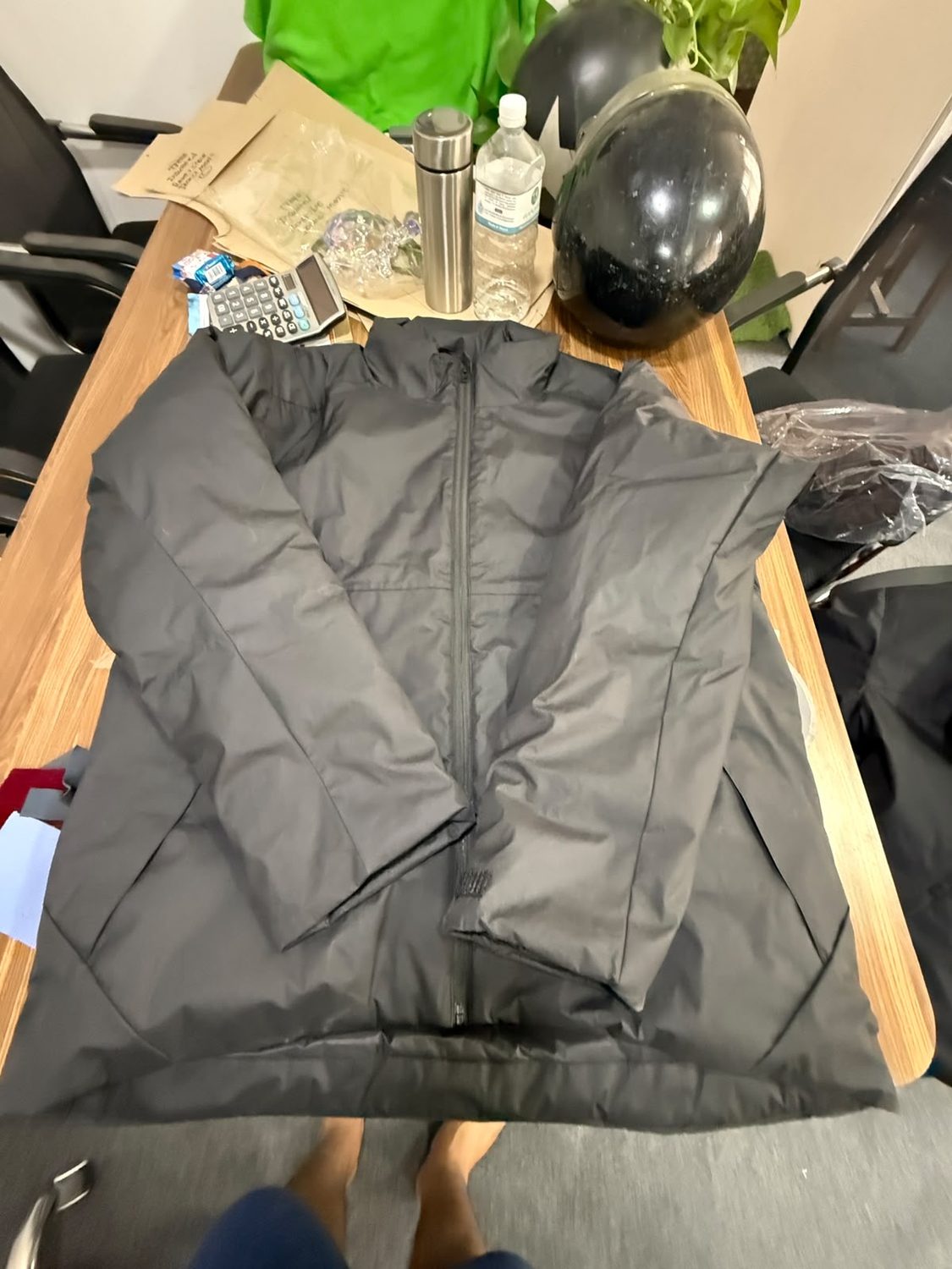 A dark grey insulated jacket held open on a workroom table